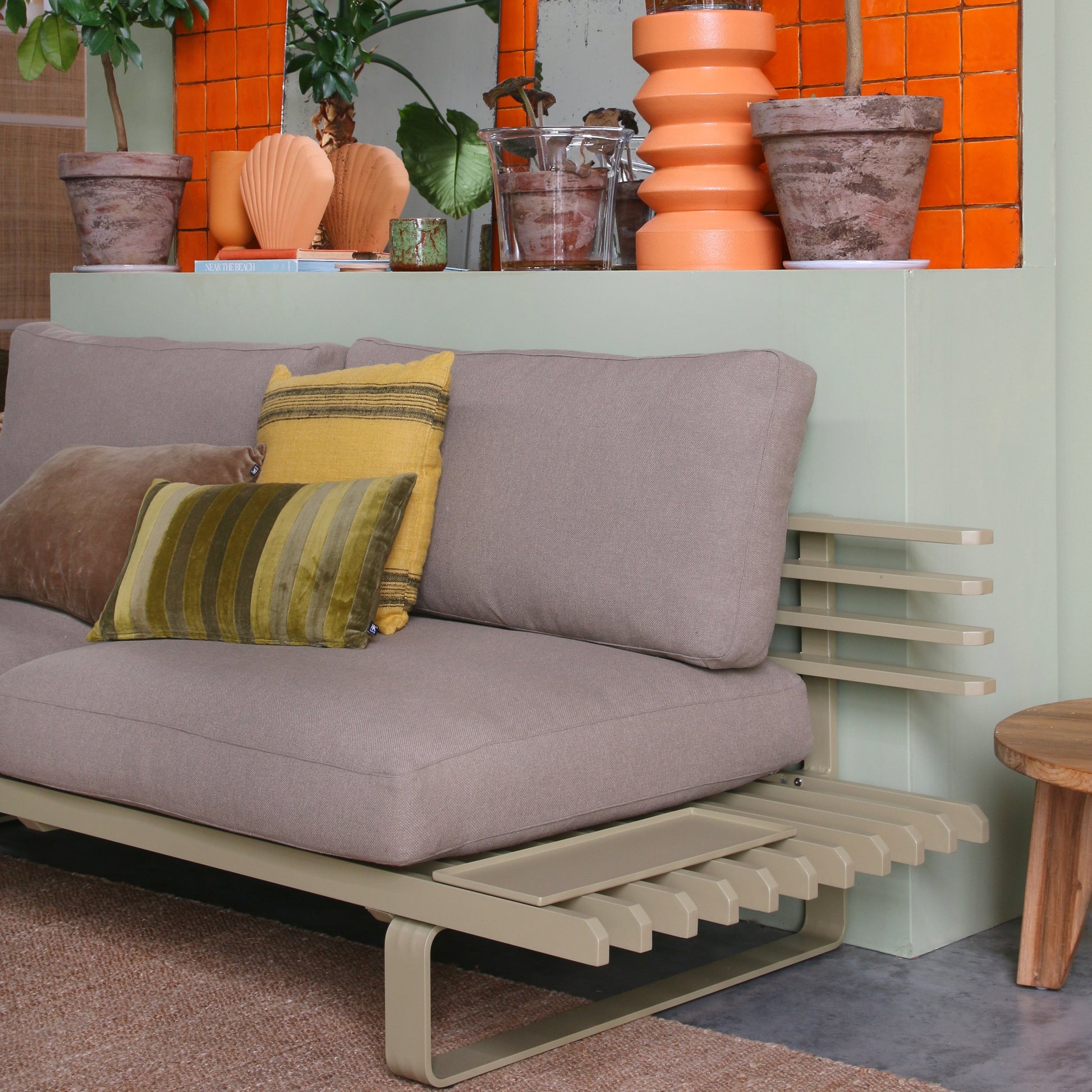olive green aluminum sofa frame with brown seating against a green wall with orange accessories 