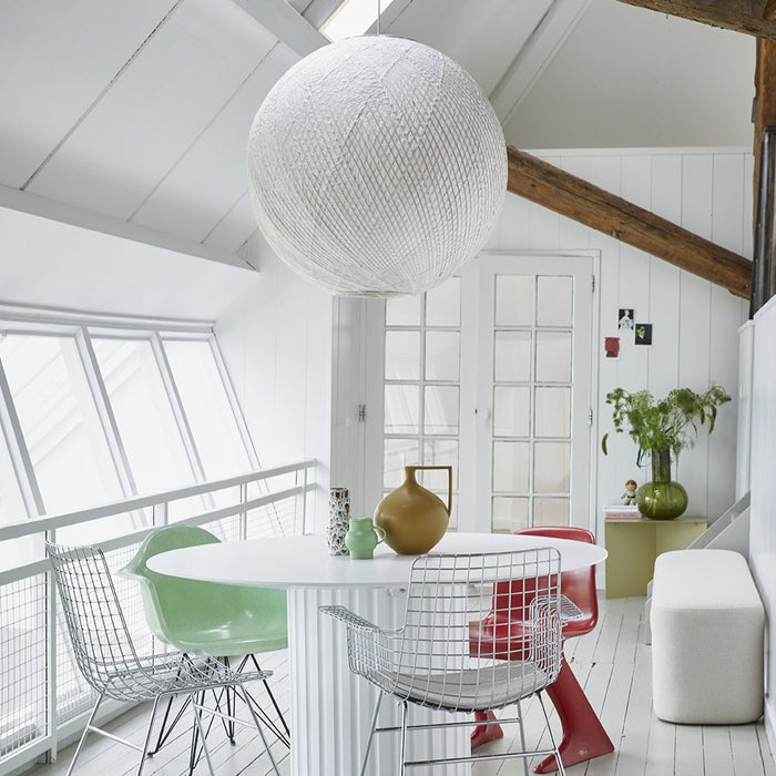 light room with white walls, white ceiling, white table and large white hanging ball lamp in combination with chrome chairs and one red and one green chair