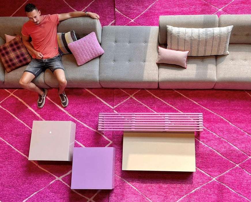 birdeye view of pink rugs and block tables and a hot pink slatted wooden bench with man sitting on beige element sofa