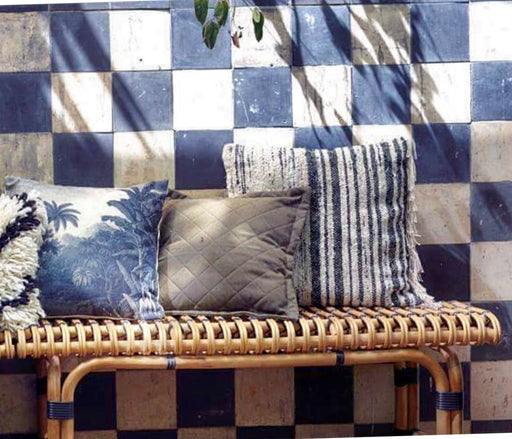 blue and white tile wall with a rattan bench filled with throw pillows in different colors and prints
