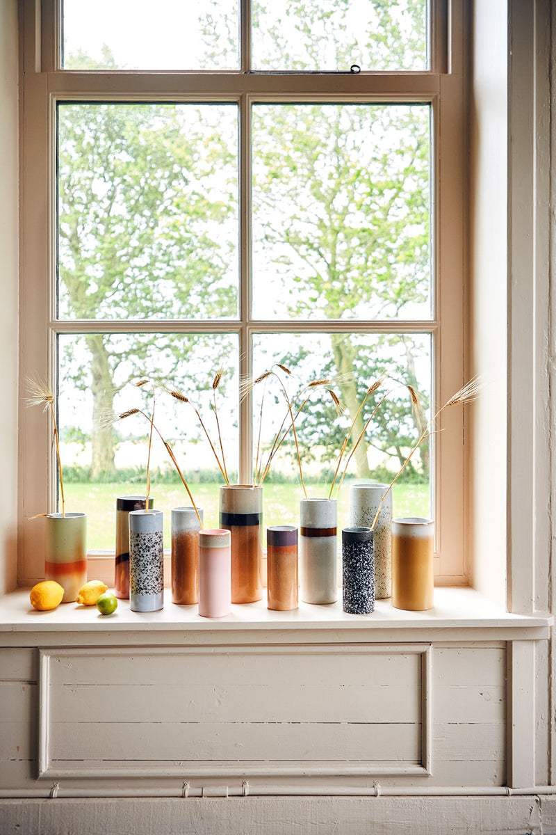 tall window with a group of stoneware retro style flower vases in various colors