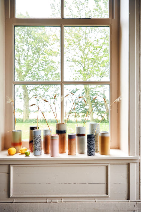tall window with a group of stoneware retro style flower vases in various colors