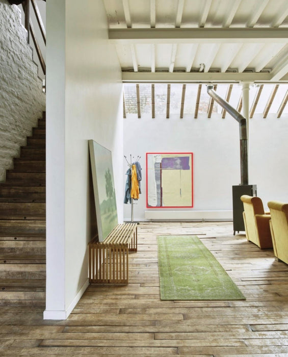 staircase and open living room with wooden flooring green runner, a teak wooden slatted bench and a large abstract painting with a neon pink frame on wall.