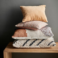 textured lumbar and accent pillows stacked on a teak wooden bench against a dark grey wall