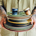 tattooed man holding a stack of ceramics