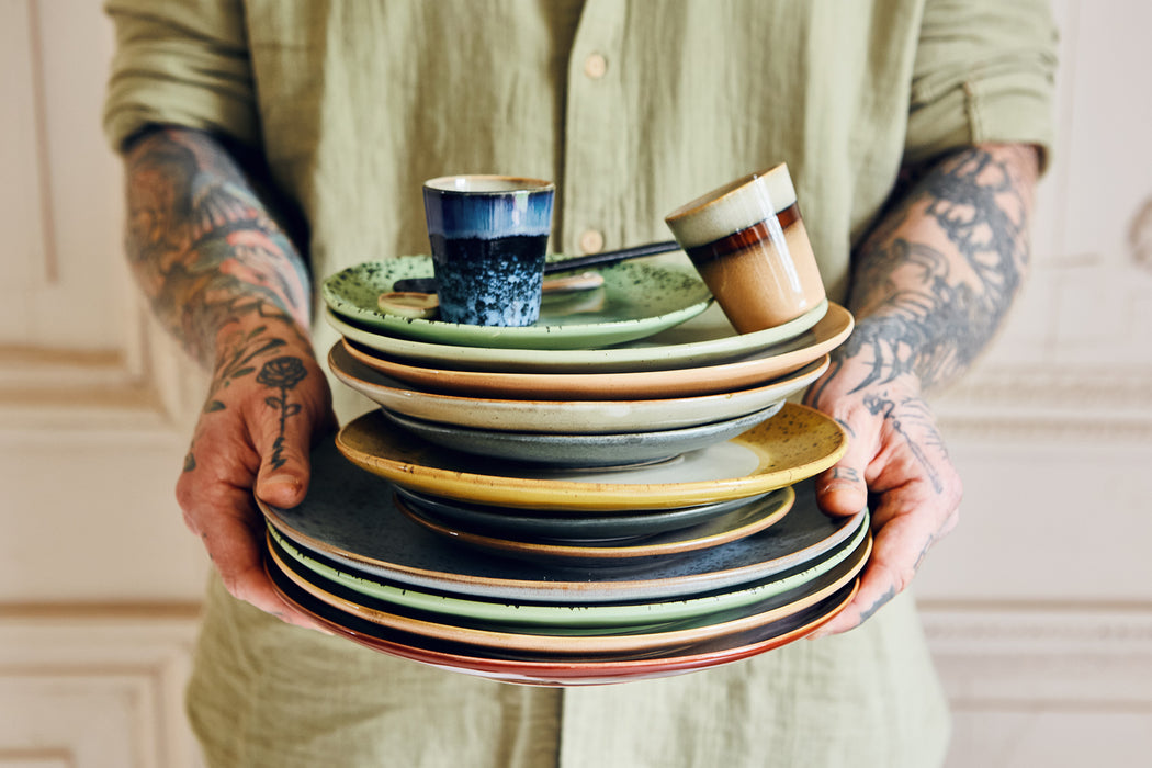 guy with tattoos holding stack of dinnerware 
