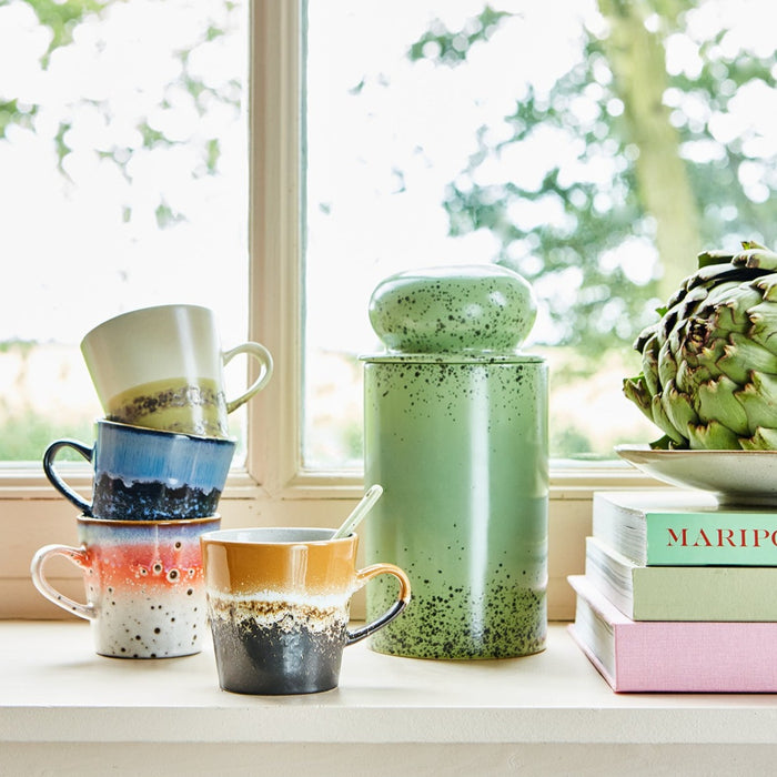 green storage jar in window with colorful mugs