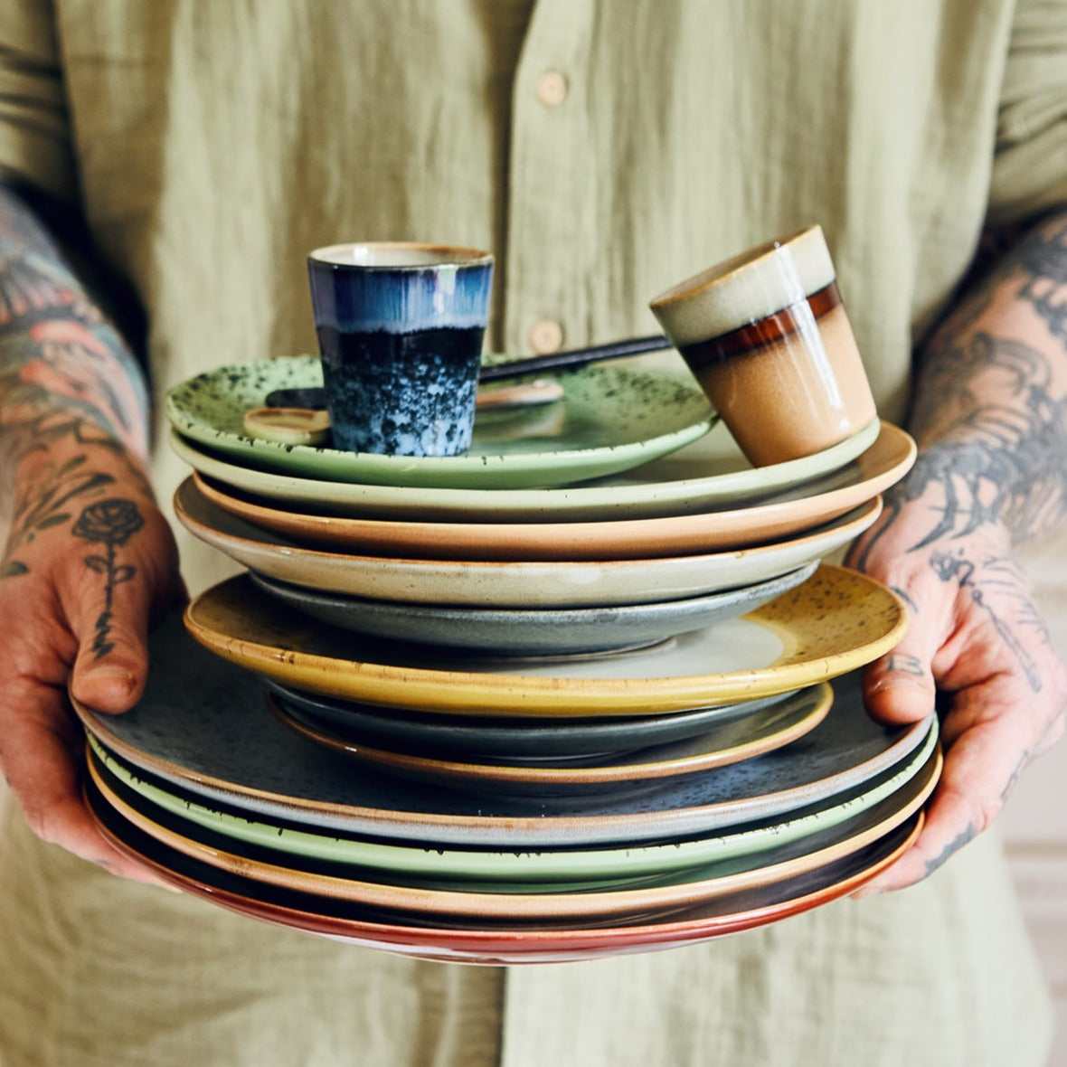 stack with stoneware plates hold by tattooed hands 