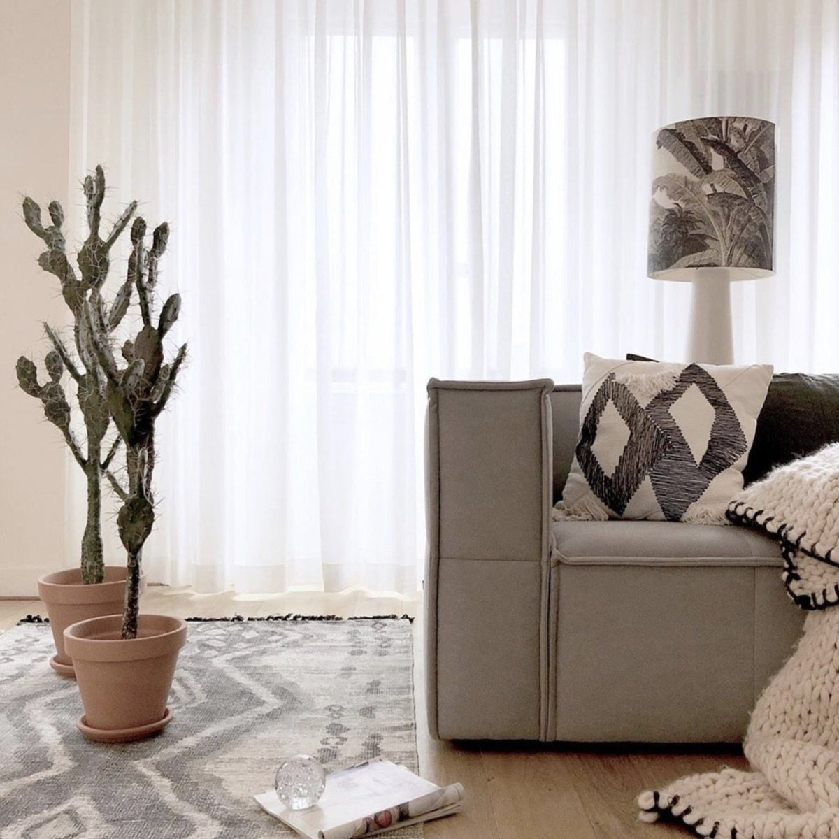 grey couch with table lamp on grey base behind it next to some pots with plants