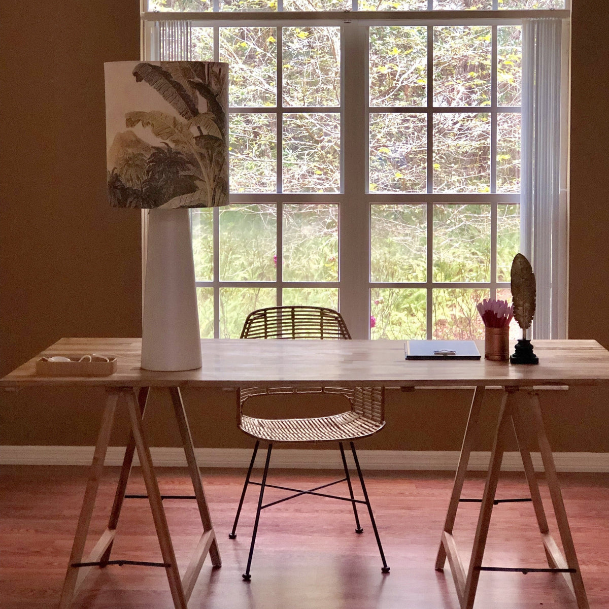 desk in front of a window with a large table lamp with jungle print shade and grey base in cone style