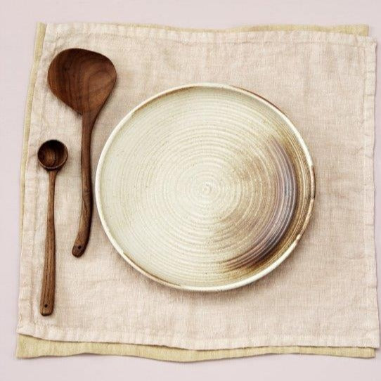 two wooden spoon and a plate in earth tones on a linen napkin