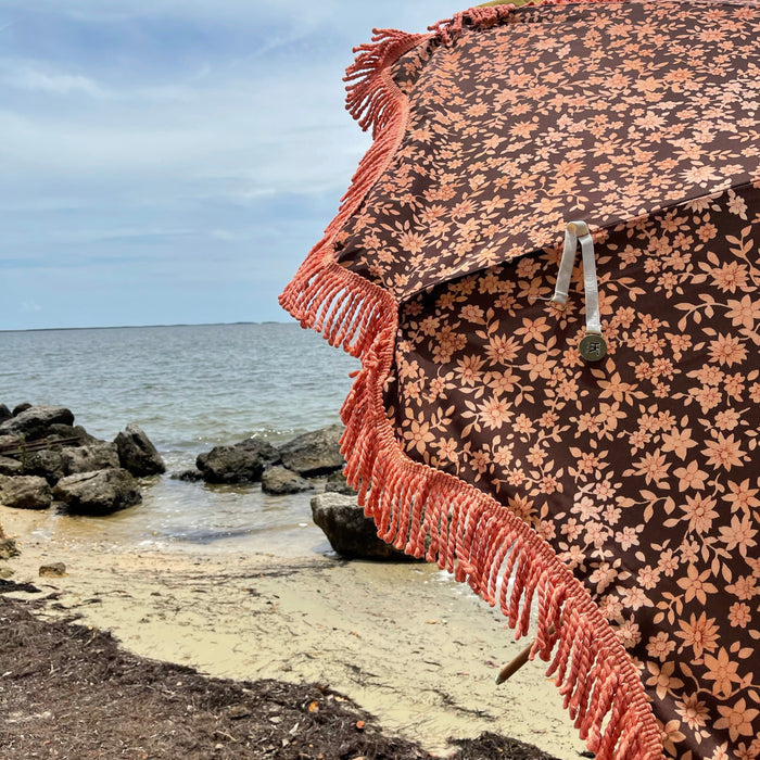 detail of retro style beach umbrella with printed floral fabric and orange fringes