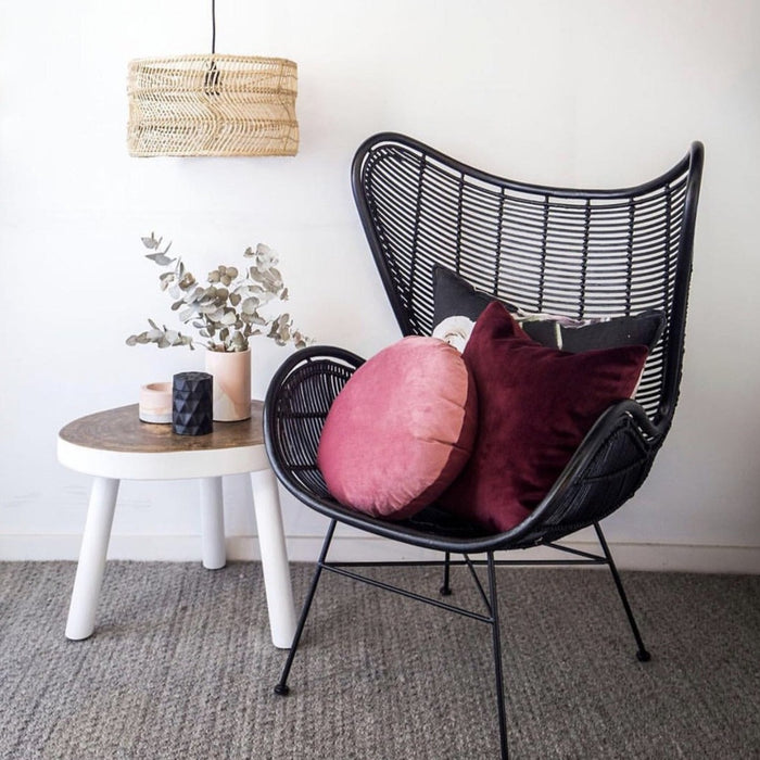 black rattan egg chair with maroon colored pillows and a natural and white tree table