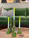 green ceramic candle stick holders with bright yellow and green and blue twisted candle on a wicker coffee table