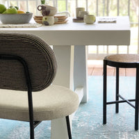 dining bench in blac and white and grey fabric with a white, wooden dining table with dinnerware in pastel colors