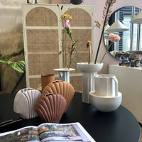 cane webbing cabinet and black table filled with stoneware flower vases that look like Greek columns 