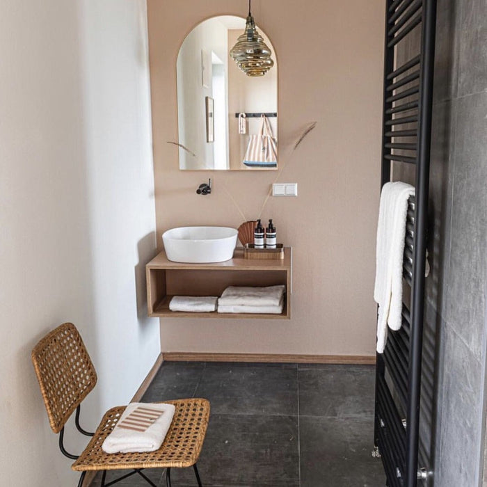 bathroom with natural rattan desk chair and arch shaped mirror