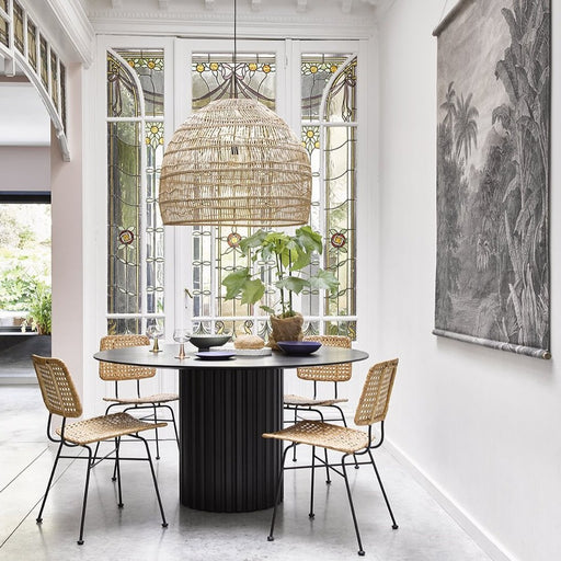 large natural wicker basket light hanging over a black pillar dining table with 4 natural wicker desk chairs 