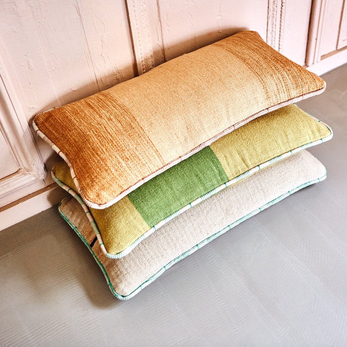 stack of 3 hand woven woolen lumbar pillows in orange, green and taupe with white piping