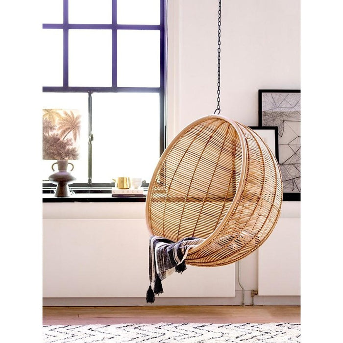 rattan hanging bowl chair and table lamp with jungle print in window.